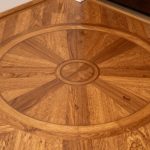 Detailed close-up of an intricate wood floor medallion in an entryway, warm oak tones, visible inlay grains
