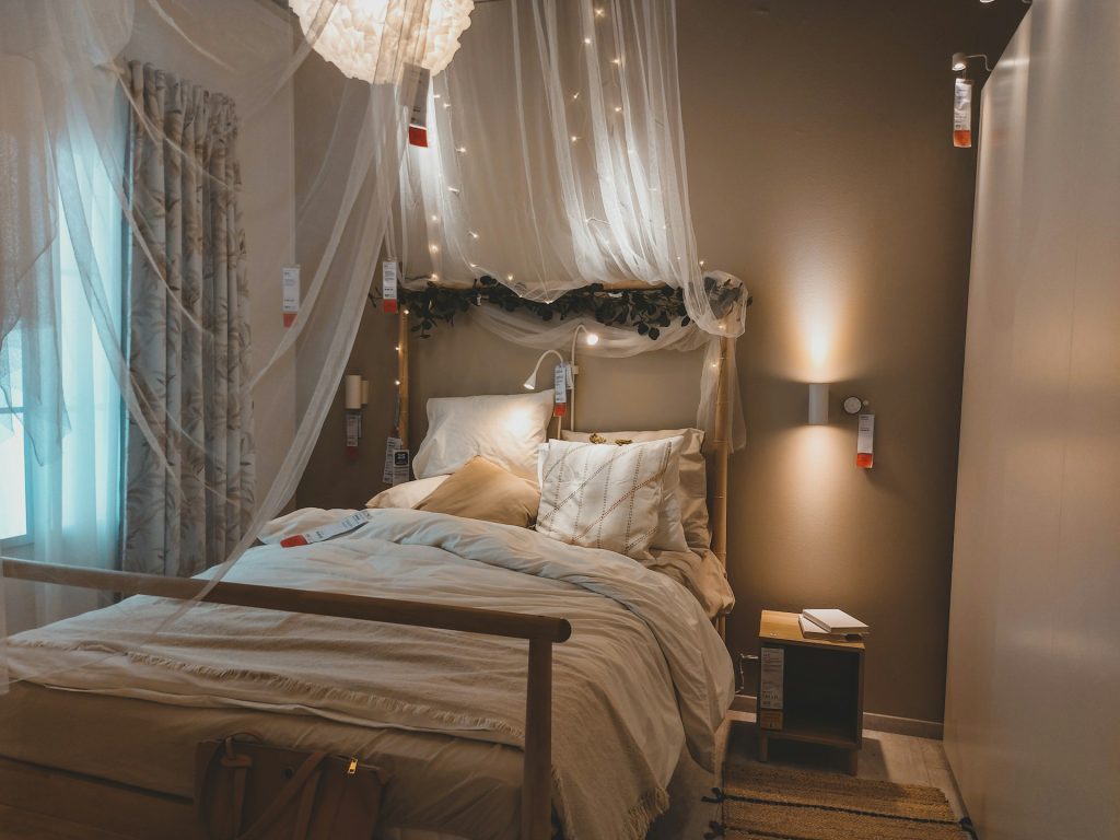 A cozy bedroom with soft bedding, a wooden bed frame, warm lighting, and minimalist décor on the nightstand