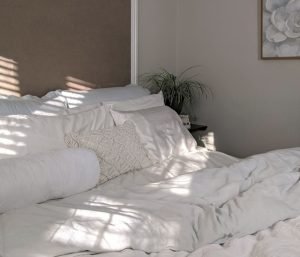Person making bed in cozy modern hotel-inspired bedroom with white bedding and warm neutral palette