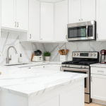 A modern renovated kitchen with white cabinets, marble countertops, and stainless steel appliances — bright, clean, and elegant.