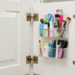 A bathroom cabinet door fitted with a clear over-the-door organizer holding small toiletries and grooming tools.